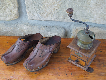 old antique hand coffee grinder and leather clogs on old wooden desk with sandsotone wall backgroundの写真素材