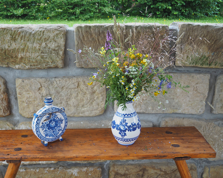 demotic  white blue painted pottery flask and vase with field flowers ond sandstone wall backgroundの写真素材