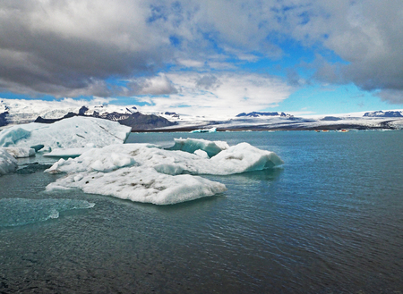 Blue ice block in glacier ice in the Jokulsarlon lagoon in south eastern Iceland blue sky and dark cloudsの写真素材