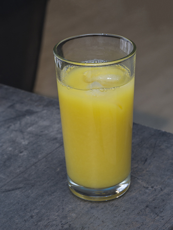 glass of orange juice with ice cube on the grey desk with grey backgroundの写真素材