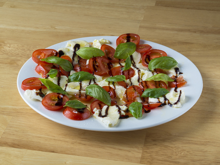 italian caprese salad on white plate  tomatoes basil an mozzarella on wooden deskの写真素材
