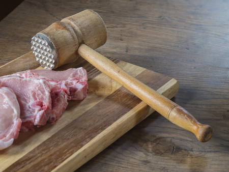 fresh raw pork chops  meat with old meat mallet on chopping board on wooden deskの写真素材