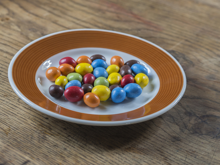colorful bonbon candy on white brown plate on wooden deskの写真素材