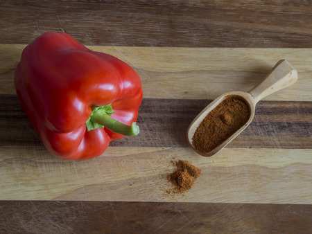 close up perfect red sweet pepper  with spice pepper in small wooden scoop spilt on wooden chopping boardの写真素材