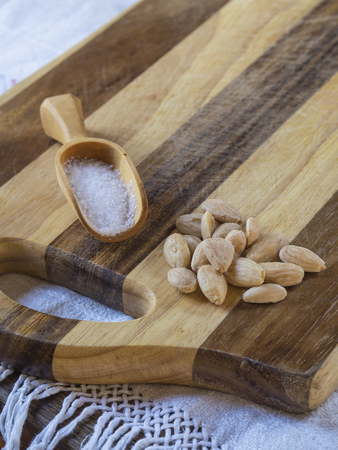 salted almonds with wooden scoop with salt on wooden cutting board on white tableclothの写真素材