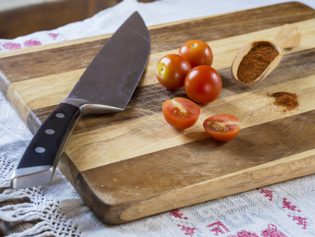 three and two half of cherry tomatoes with kitchen knife and scoop with red pepper spice on wooden...