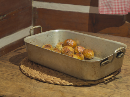 whole baked potatoes in rustic baking pan on wooden table in timbered farmhouseの写真素材