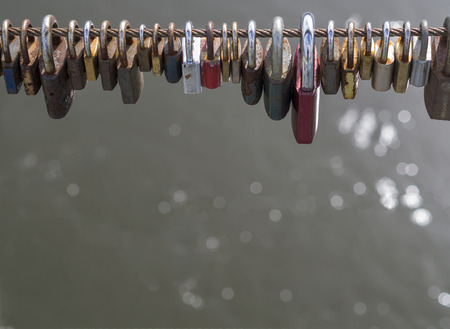 colorful locks hanging from high wire of bridge with bokeh lights on gray water backgroundの写真素材