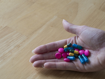 women hand full of colorful blue green yellow and pink pills pain killers and antibiotic capsule wooden backgroundの写真素材