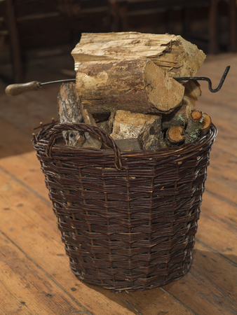 wicker basket full of chopped wood and fire-hook  on wooden board floorの写真素材