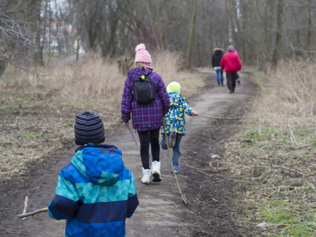 three children in colorful jacket holding stick and his parents on the walk in Prague hostivar forest park in late winter, view from behind, selective focusの写真素材