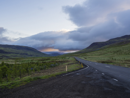 Asphalt road curve through empty northern landscape with green grass colorful hills and sunset dramatic sky, way to the mountains in Iceland western highlands, copy spaceの写真素材