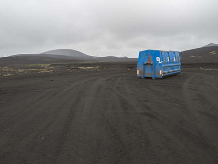blue metal garbage container standing alone in black lava sand desert in Iceland, hills and gray sky background, copy spaceの写真素材