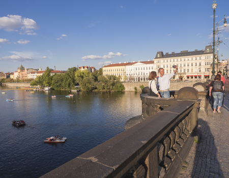 Czech Republic, Prague, September 8, 2018: Middle age couple taking selfie picture on Legion Bridge with view on Vltava river and Old Town, golden hour light, tourists relaxing on pedal boatsのeditorial素材