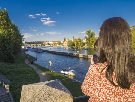 Czech Republic, Prague, September 8, 2018: young woman, taking picture with her cell phone from Legion Bridge with view on Kampa island, Vltava river, Prague Castle, Old Town, summer sunny afternoonのeditorial素材