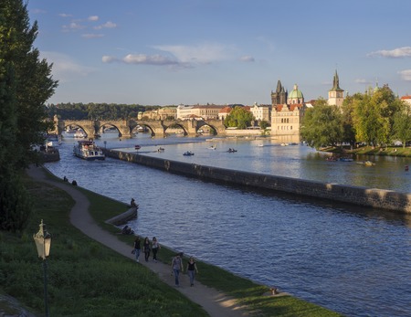 Czech Republic, Prague, September 8, 2018: Kampa island with view of Prague Old Town, Charles bridge, Vltava river, steamers, walking people and tourists on pedal boats. Golden hour light, summer.のeditorial素材