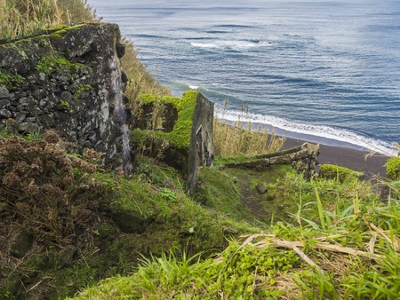 Abondoned ruin remains of house at Praia da Viola beach, covered by moss and grass, lush vegetation at bank of atlantic ocean, Sao Miguel island Azores island Portugalの写真素材