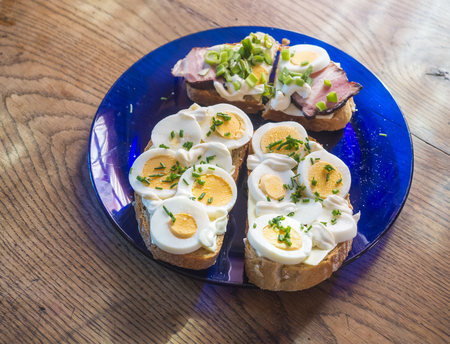 close up fresh home made rye bread sandwich with egg slices, ham bacon, chive and mayonnaise on blue...