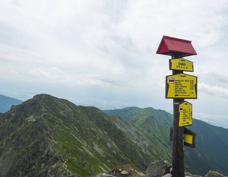 Trail signpost at Top of the peak Banikov at Western Tatra mountains or Rohace. Sharp green mountains with hiking trail on ridge. Summer blue sky white clouds.の写真素材