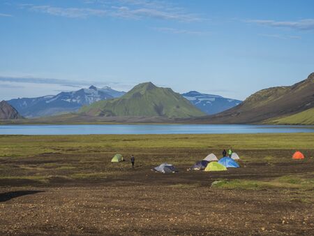 Colorful tents at camping site on blue Alftavatn lake with green hills and glacier in the otherwordly beautiful landscape of the Fjallabak Nature Reserve in the Highlands of Iceland part of famous Laugavegur hiking trail.の写真素材