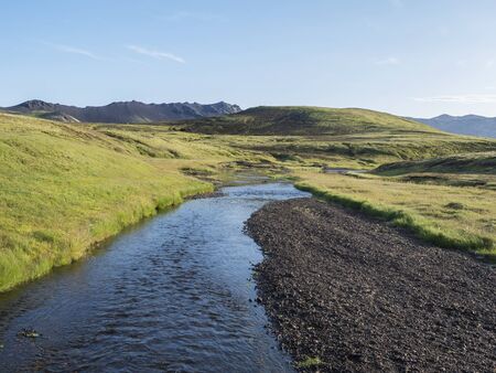 Volcanic hills, lush grass and blue river next to camping site on Alftavatn lake. Summer sunny day,...