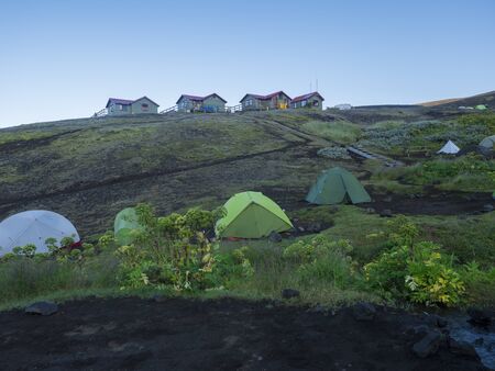 Colorful tents and Botnar mountain hut at Iceland on Laugavegur hiking trail, green valley in...