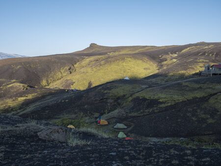Colorful tents and Botnar mountain hut at Iceland on Laugavegur hiking trail, green valley in...
