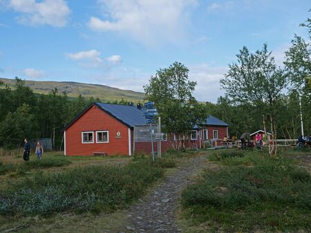 Abiskojaure, Norrbotten, Sweden, Agust 23, 2019: group of hikers resting at red AbiskoJaure STF hut. Green hills, birch forest and flowing river and lake Abiskojaure on the Kungsleden Trail.のeditorial素材