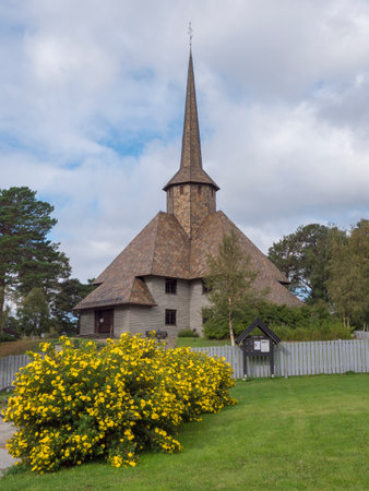 The old church of Dombas in traditional style with blooming yellow flowers. Blue sky, white cloud background. Oppland, Norway.の写真素材