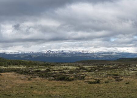 Autumn view on hills and snow capped mountains with dramatic clouds at Dovre Nasjonaalpark nature park from main road E6, Norway.の写真素材