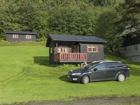 Storen, Norway, September 7, 2019: View of Classical Norwegian Camping site with traditional wooden cabins, lush green grass and trees. Black car parked in front of cottage, Central Norway.のeditorial素材