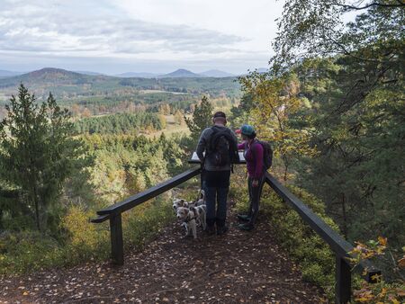 CZECH REPUBLIC, SLOUP V CECHACH, October 27,2019: Men and woman couple with two dogs at view on village Sloup v cechach with mediaval sand stone castle in luzicke hory, Lusatian Mountains with autumn colored tree forest and green hillsのeditorial素材