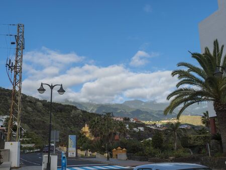 Los Cancajos, La Palma, Canary Islands, Spain, December 22, 2019: Main street of Los Cancajos with view on green mountains and hills, parked cars and palm treesのeditorial素材