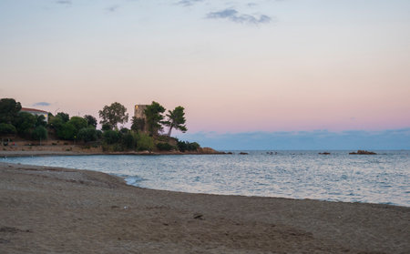 view of empty Spiaggia di Santa Maria Navarrese sand beach with green trees and old stone tower Torre Saracena in village Santa Maria Navarrese, Sardinia, Italy. Golden hour lightの写真素材