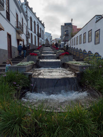 Firgas, Gran Canaria, Canary Islands, Spain December 13, 2020: view of street Paseo de Gran Canaria with waterfall fountain, flowers and ceramic decorated benchesのeditorial素材
