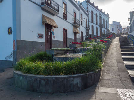 Firgas, Gran Canaria, Canary Islands, Spain December 13, 2020: view of street Paseo de Gran Canaria with waterfall fountain, flowers and ceramic decorated benchesのeditorial素材