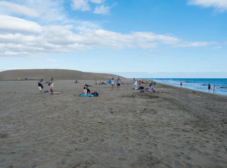 Maspalomas, Gran Canaria, Canary Islands, Spain December 18, 2020: Group of tourist people sunbathing at beach at Natural Reserve of Dunes of Maspalomas, golden sand dunes, blue sky.のeditorial素材