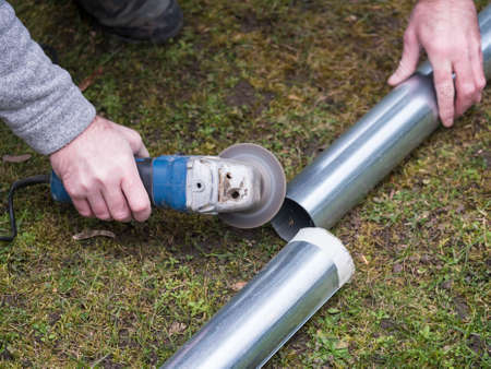 hands of man cutting the stove pipe, working with portable grinder machine on the grassの写真素材