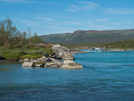 View of turquoise blue water of wild Vuojatadno river. Northern landscape in Swedish Lapland with...