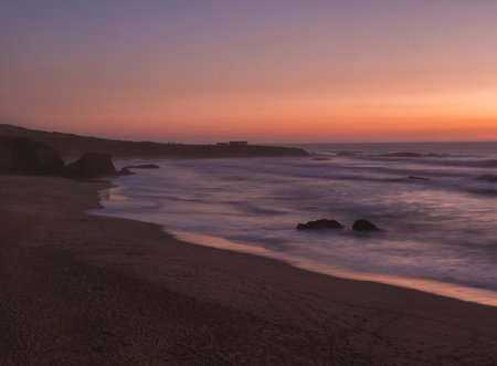 Mysterious long exposure view of sand beach Praia Grande de Almograve with blurred ocean waves in pink orange and purple light. Blue hour after sunset at Rota Vicentina coast, Almograve, Portugalの写真素材