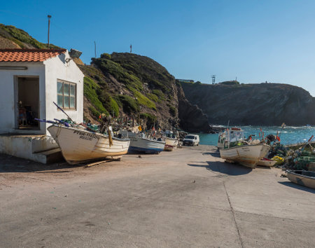 Zambujeira do Mar, Odemira, Portugal, October 27, 2021: fishing house and old rusty boats at small fishing port Entrada da Barca with surrounding cliffs and clear blue sky.のeditorial素材