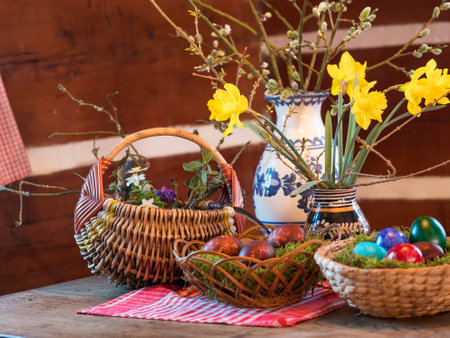 Easter and spring still life with wicker baskets, coloured decorated easter eggs ,moss, feather, vases flowers with narcissus on rustic wooden table in log cabin. Happy Easter holiday cardの写真素材