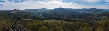 Wide panoramic view from viewpoint Stredni vrch near Dolni Prysk, Ceska Kamenice. Autumn landscape with colorful forest, hills and blue cloudy sky in Luzicke hory Lusatian Mountains, Czech Republic.の写真素材