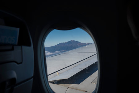 Window view from an airplane with wing of an airplane and Pico del Teide volcano. Flight over Tenerife, Canary Islands. Blue sky background, copy spaceの写真素材
