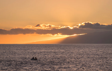 Orange sunset at sea shore promenade in Playa de San Juan, Tenerife, Spain with fisherman boatの写真素材