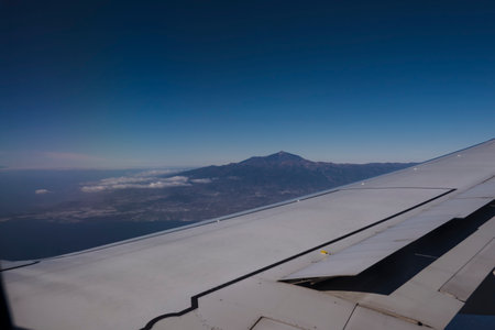 Window view from an airplane with wing of an airplane and Pico del Teide volcano. Flight over Tenerife, Canary Islands. Blue sky background, copy spaceの写真素材