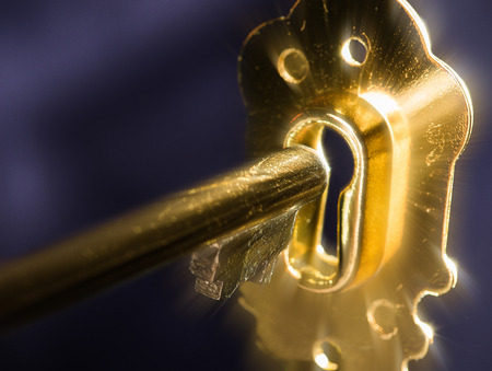 A golden key in a keyhole illuminated by a mysterious radiant light from the other side isolated on...