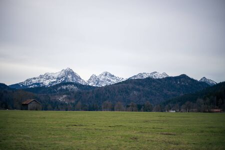 Alpine mountains with snowy peaks. Old european houses. Blue sky with clouds.