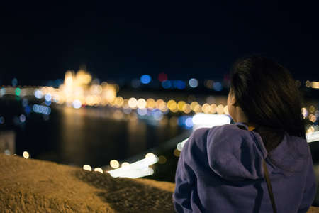 Beautiful young girl looks at the parliament building in Budapest at nightのeditorial素材