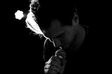 Male hand raised up with bracelets in his hands holds a microphone. Back and white photography